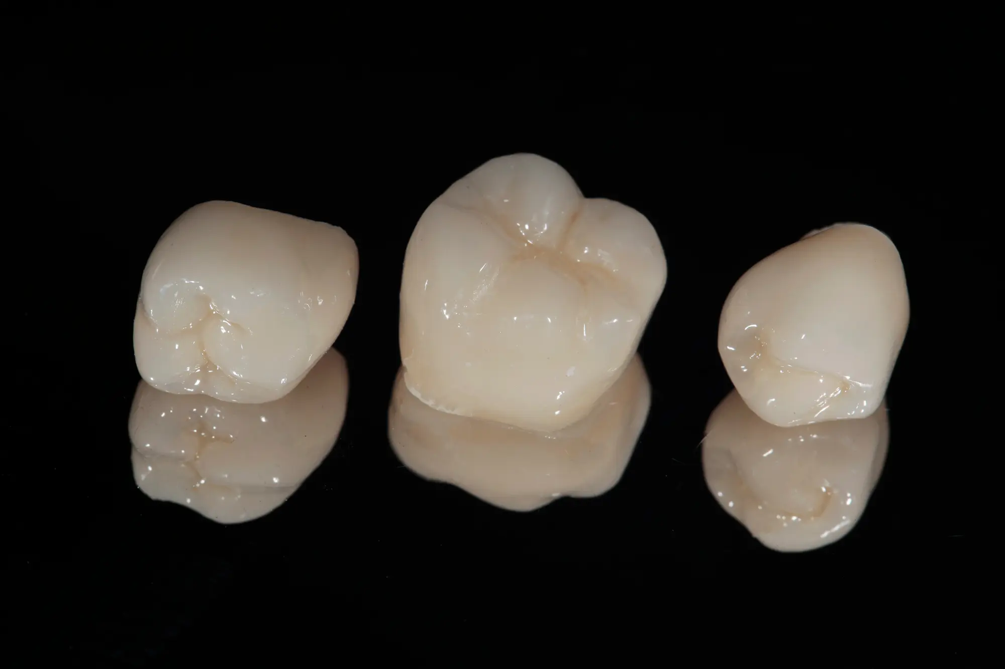 Three realistic dental crowns on a reflective black surface