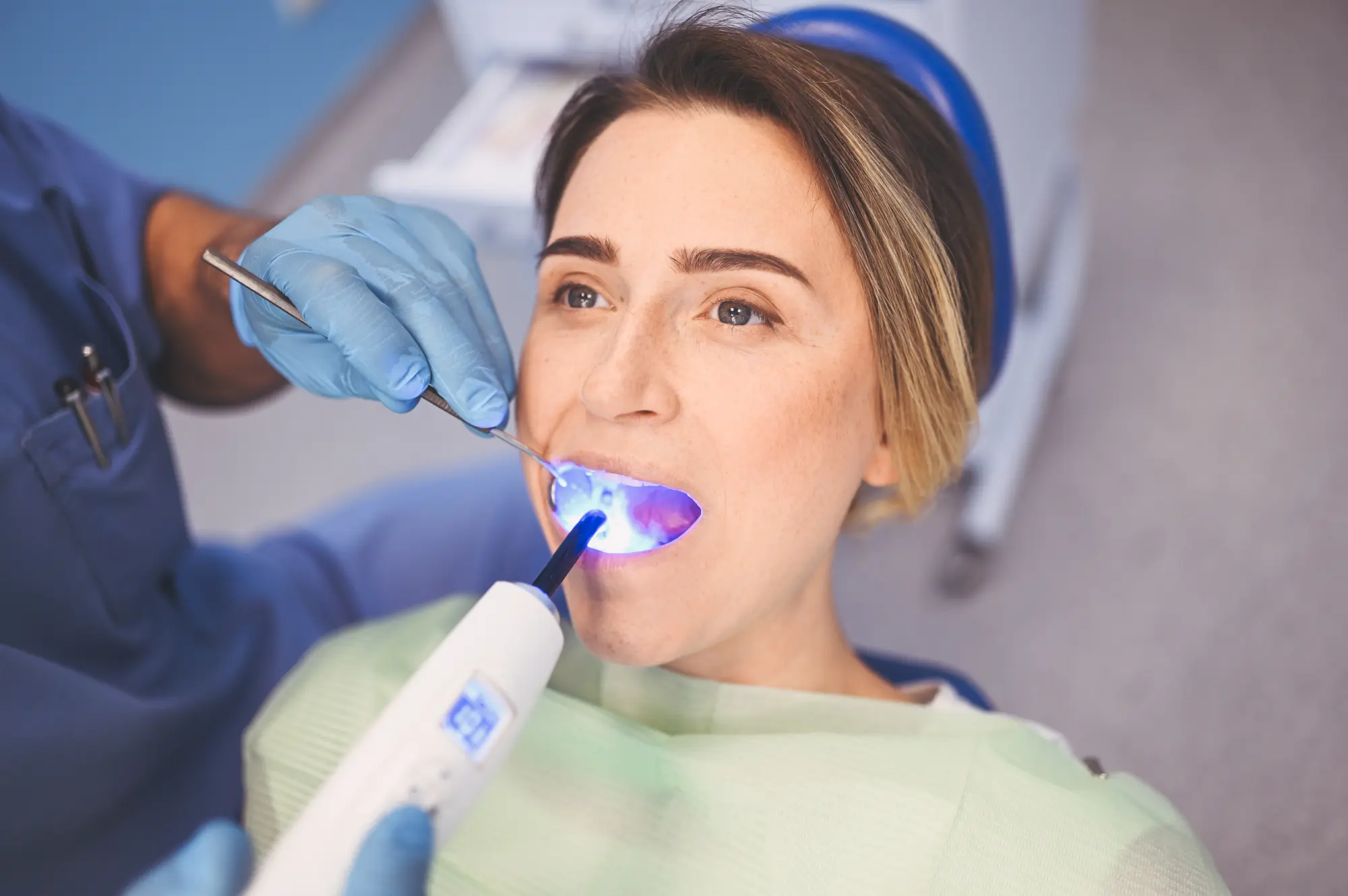 Dentist using a curing light on a patient's teeth during a dental procedure.