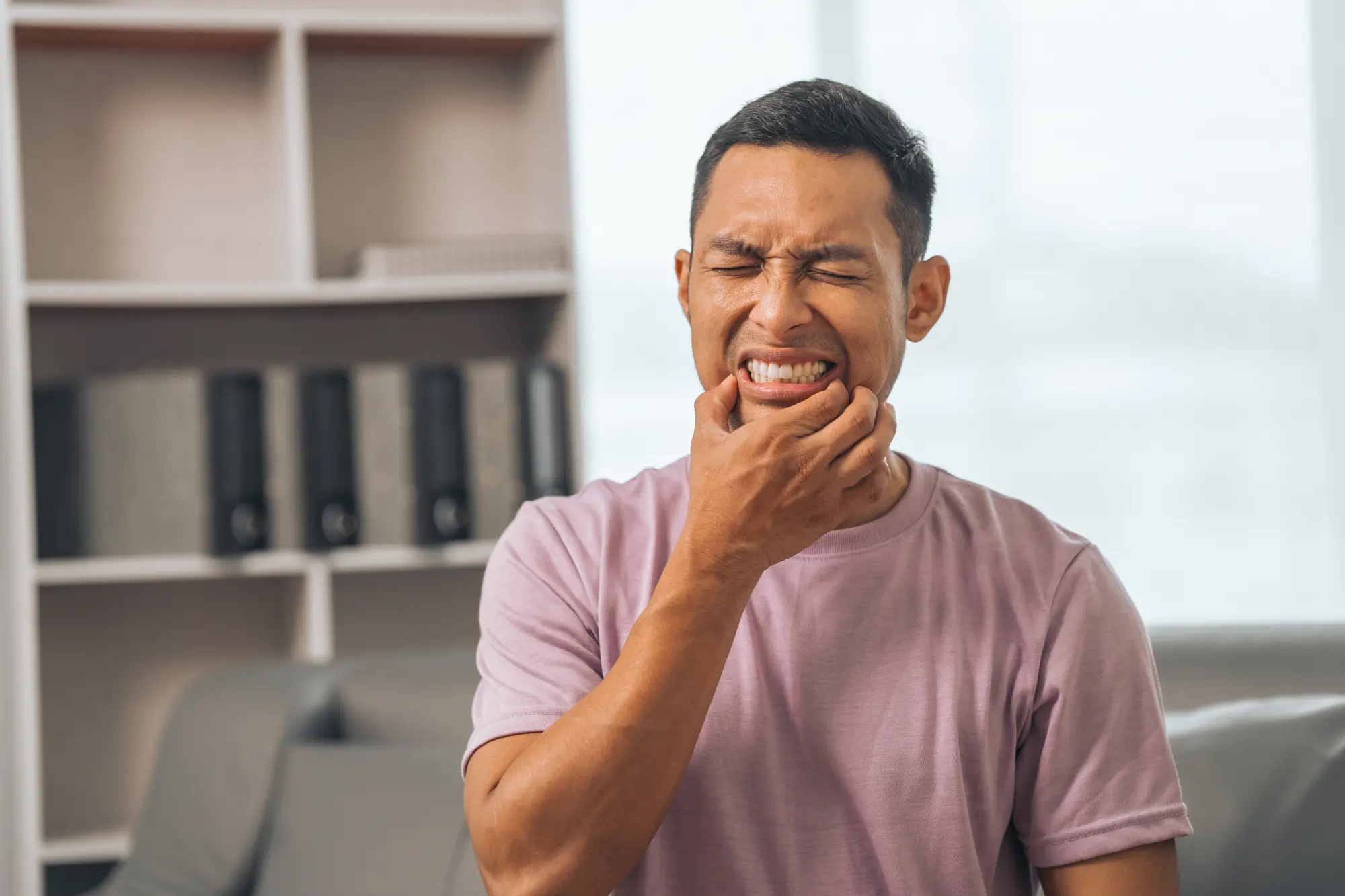 Man grimacing and holding his jaw due to toothache